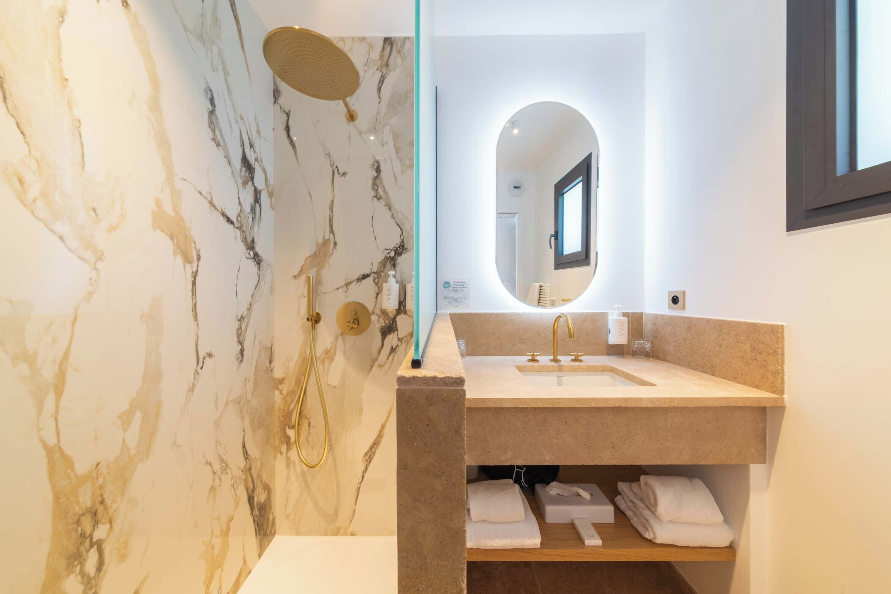 Un baño moderno con pared de mármol, lavamanos con espejo y cabina de ducha.