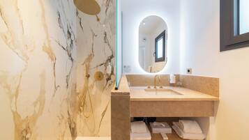 Un baño moderno con pared de mármol, lavamanos con espejo y cabina de ducha.