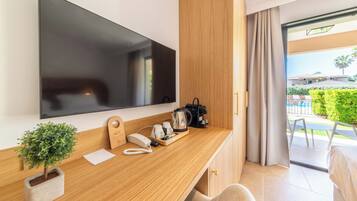 A modern hotel room with a wooden desk, a flat-screen TV, a small potted plant, a telephone, and a coffee maker.
