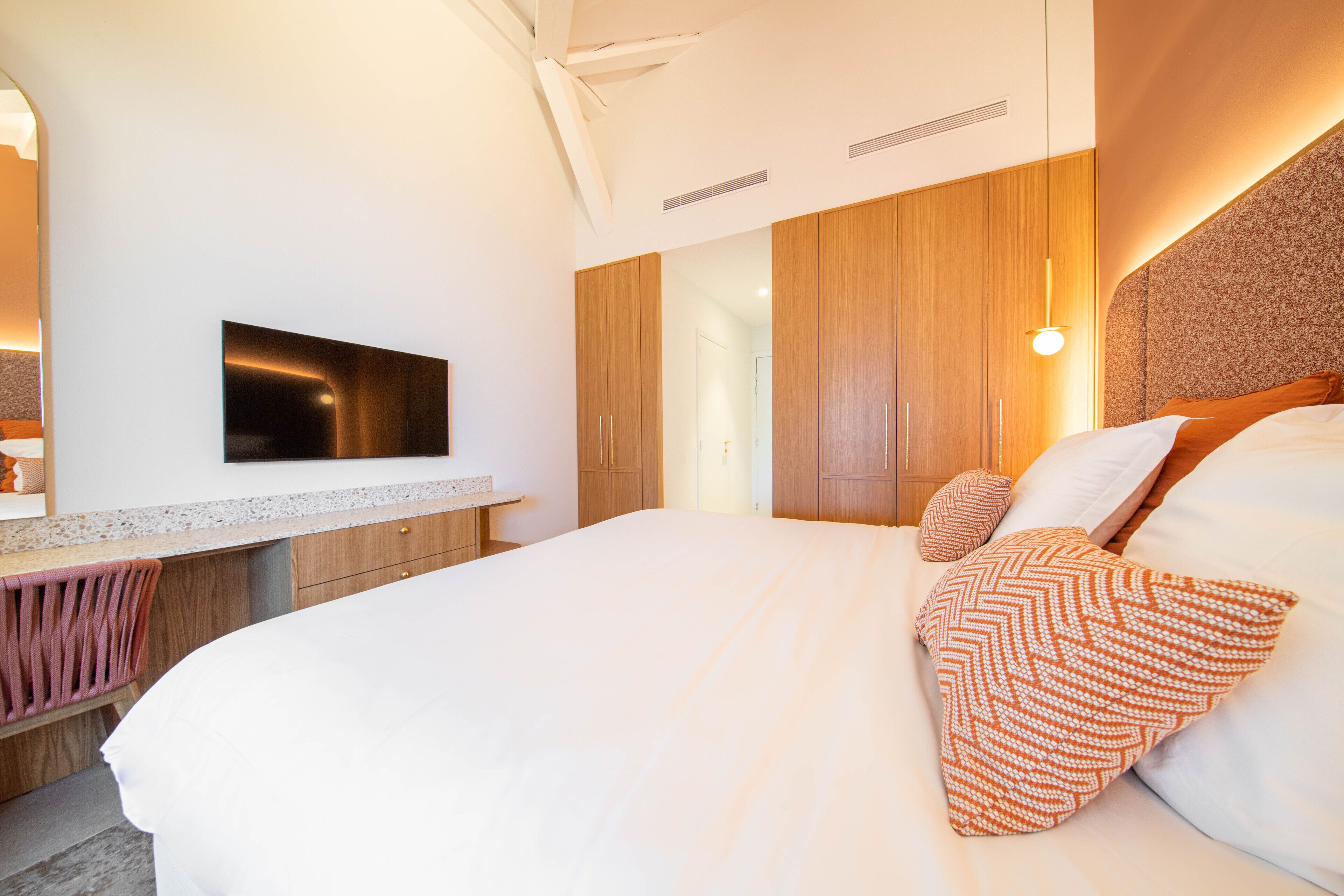 Un dormitorio moderno con una cama grande, un armario de madera y un televisor de pantalla plana montado en la pared.