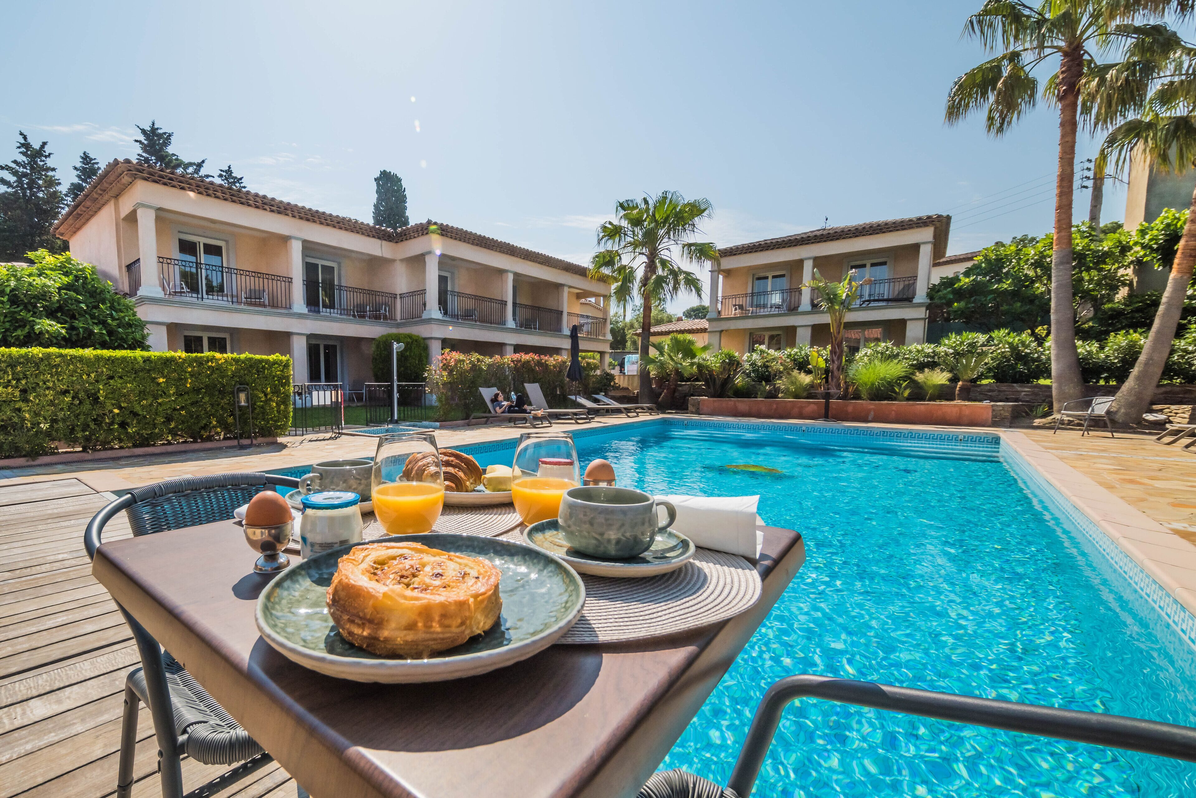 A breakfast setup by a poolside with a table, plates, and drinks.