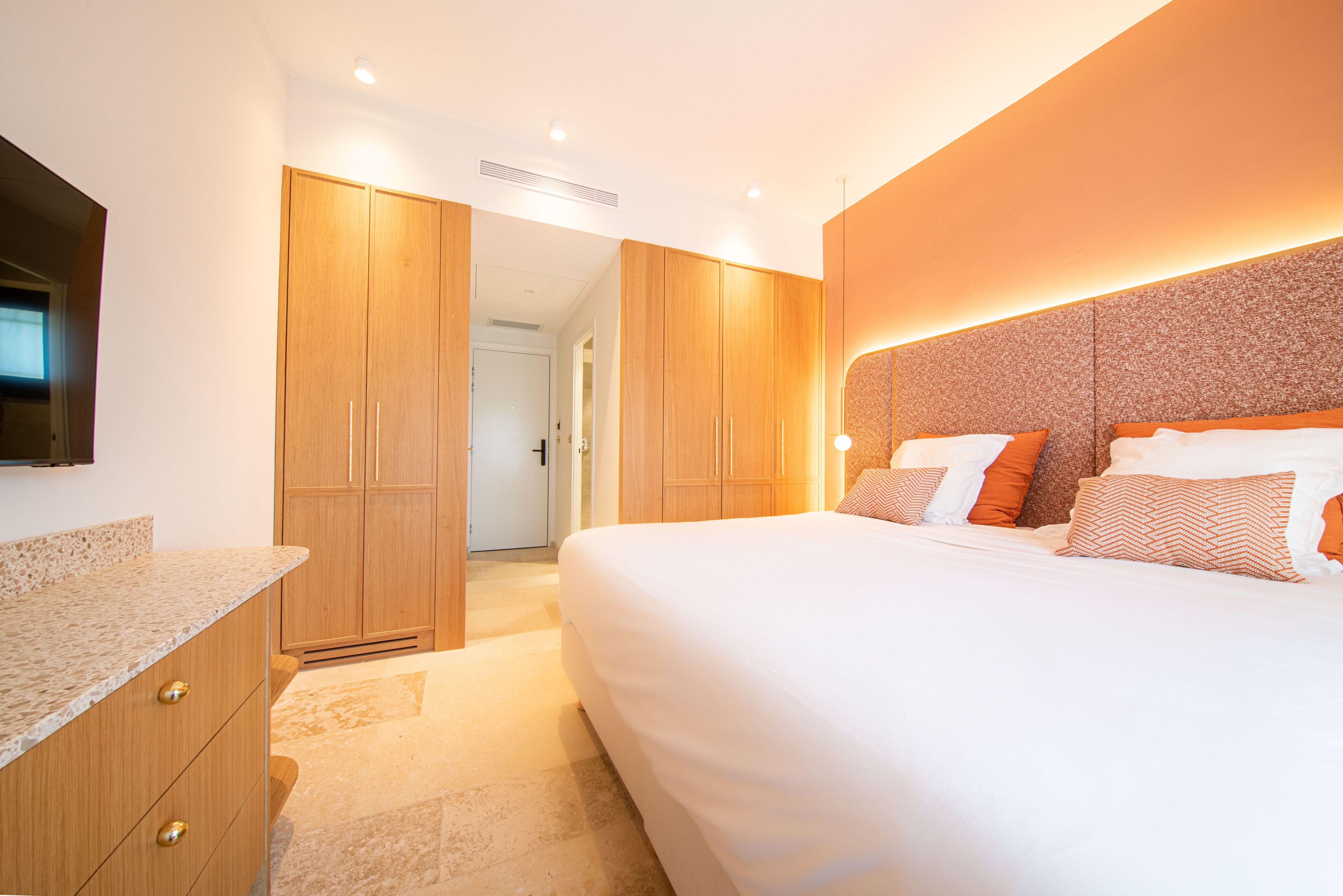 A modern hotel room with a large bed, wooden wardrobe, and a built-in TV.
