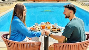 Um casal jantando à mesa perto de uma piscina, com vista para a piscina e vegetação.