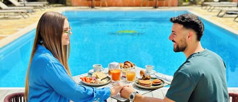 Um casal jantando à mesa perto de uma piscina, com vista para a piscina e vegetação.