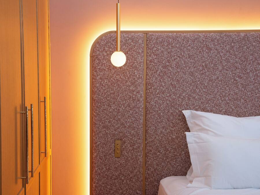 Ein modernes Hotelzimmer mit einer strukturierten Kopfteil, einem Bett mit weißen Leinen und einem minimalistischen Design.