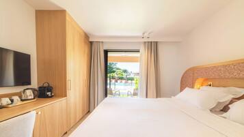 A hotel room with a bed, a desk with a television, a coffee maker, and a view of an outdoor pool area.