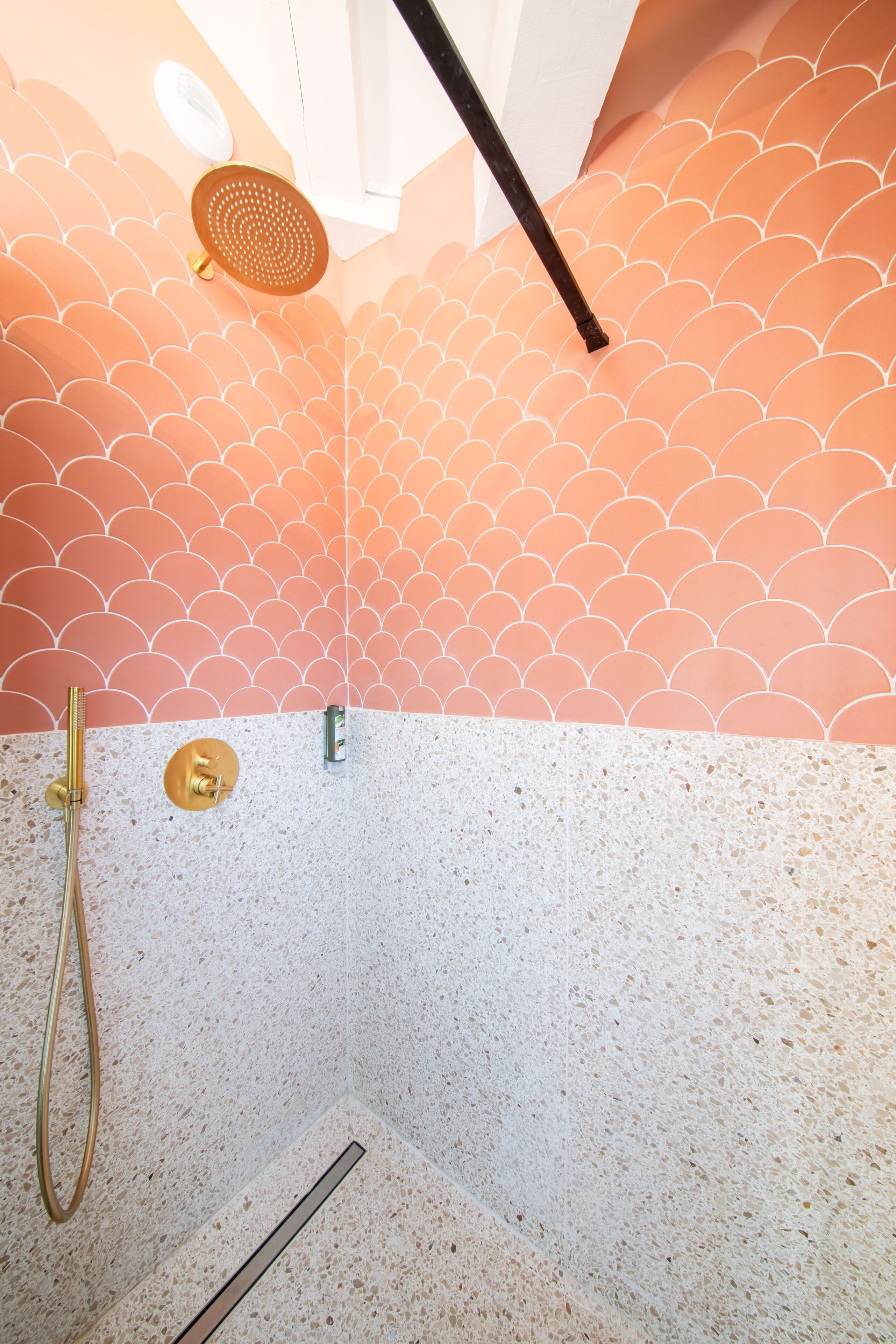 A shower with a scalloped pattern wall, a handheld showerhead, and a handheld shower attachment.