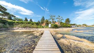 A wooden pier leading to a beach with clear water and rocky shore.