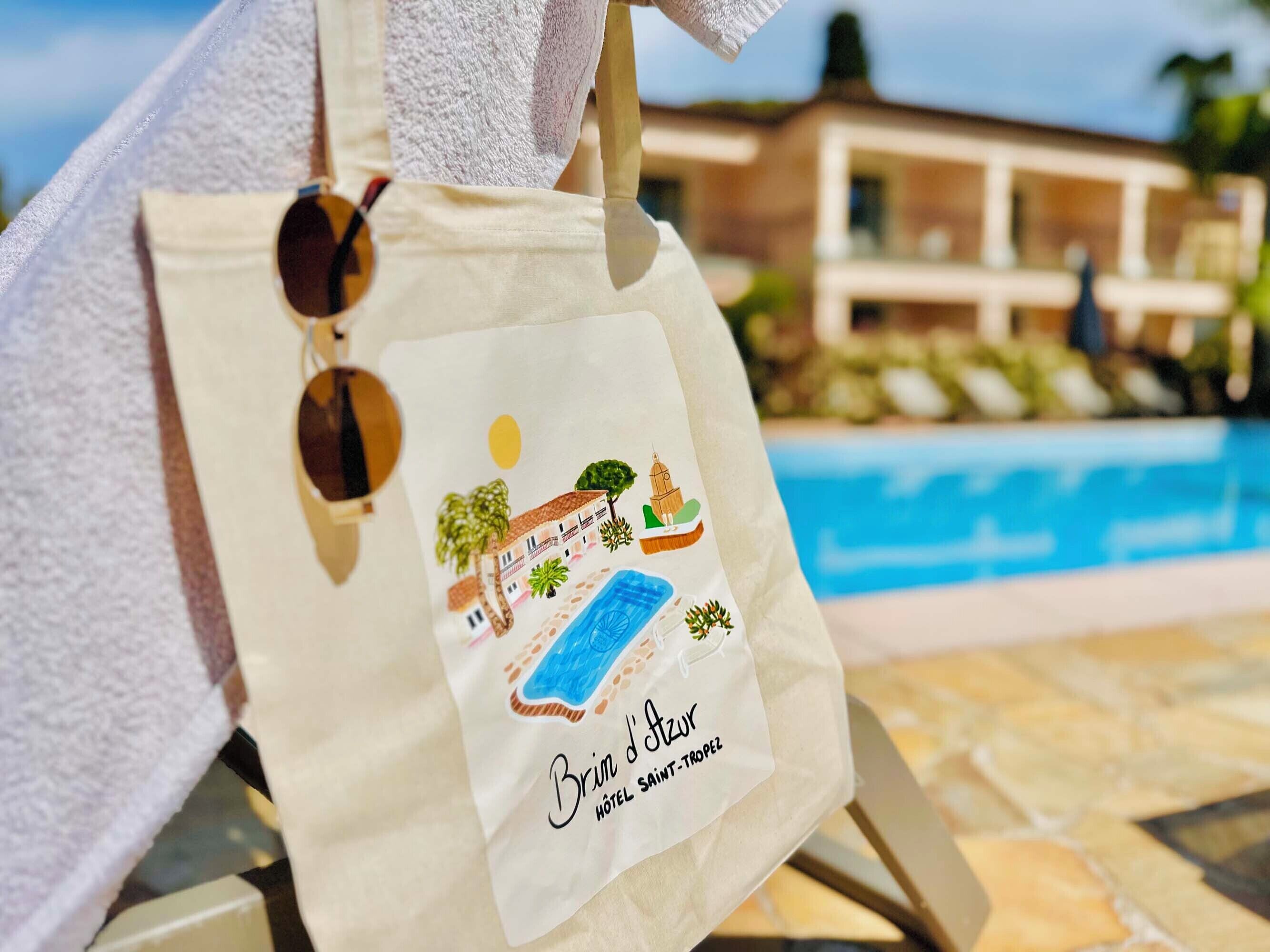 A beach towel and a tote bag with a hotel logo and a pool in the background.
