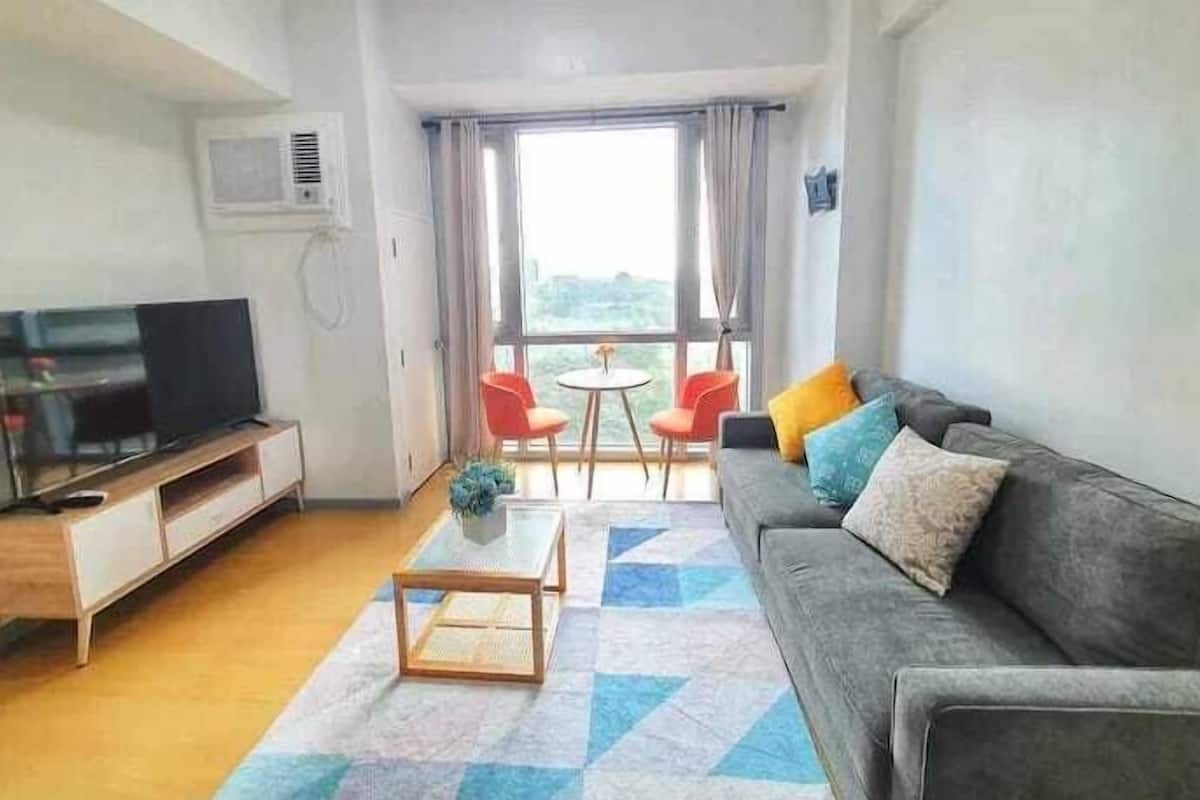 A living room with a sofa, a coffee table, a TV, and a balcony with chairs and a table.