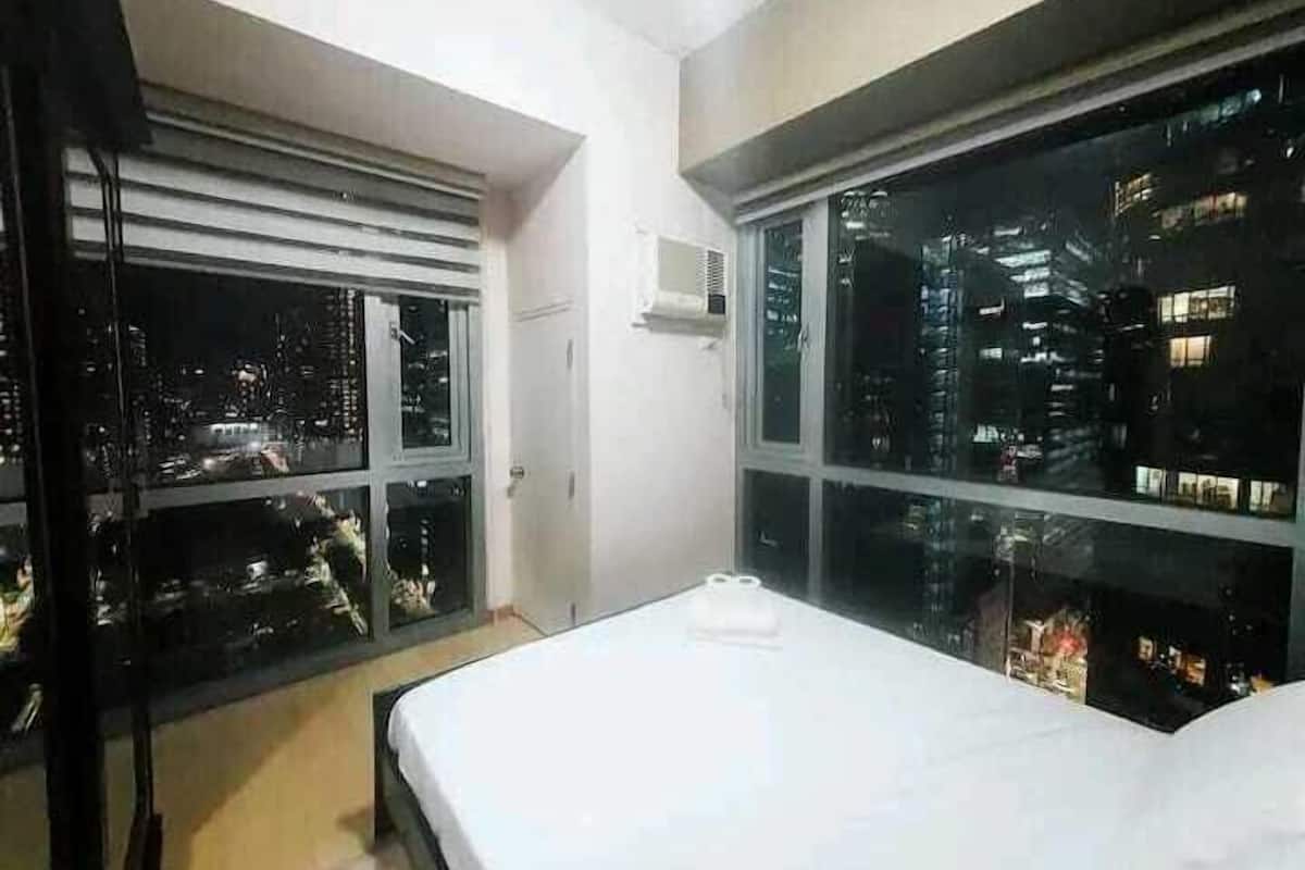 A hotel room with a large bed, a window with a city view, and an air conditioning unit on the wall.