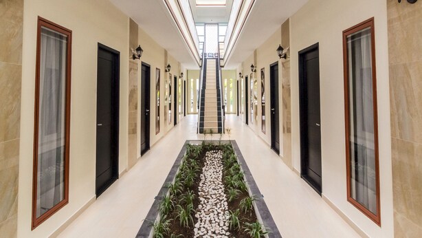 A long, narrow hallway with doors on both sides, a central garden area with plants and pebbles, and a skylight above. - OYO Life 2735 Graha Nirwana (Batam)