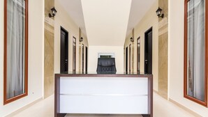 A hotel hallway with a central reception desk, multiple doors, and wall-mounted lighting. - OYO Life 2735 Graha Nirwana (Batam)