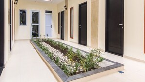 A corridor with a central garden, multiple doors, and a skylight. - OYO Life 2735 Graha Nirwana (Batam)