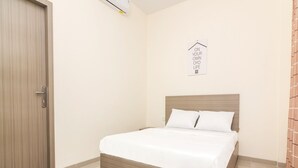 A bedroom with a wooden bed frame, white bedding, a door, a wall-mounted air conditioner, and a sign with text. - OYO Life 2735 Graha Nirwana (Batam)