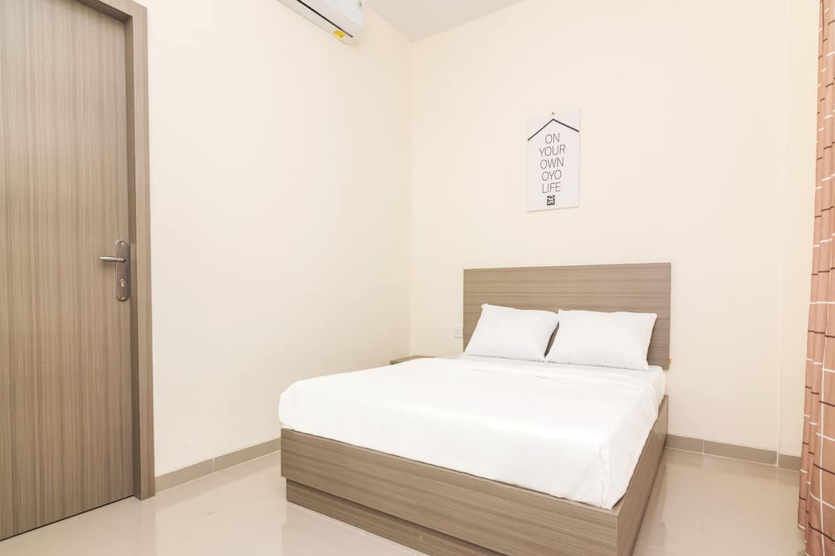 A bedroom with a wooden bed frame, white bedding, a door, a wall-mounted air conditioner, and a sign with text.