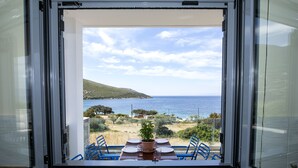 Un balcón con una mesa lista para dos personas, con vistas a un paisaje costero que incluye el mar y colinas.
