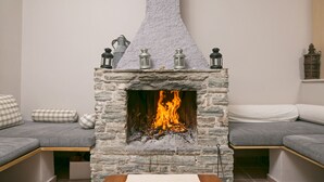 Una chimenea de piedra con fuego, flanqueada por dos sofás grises con cojines de cuadros, y una mesa de madera con una vela azul encima.