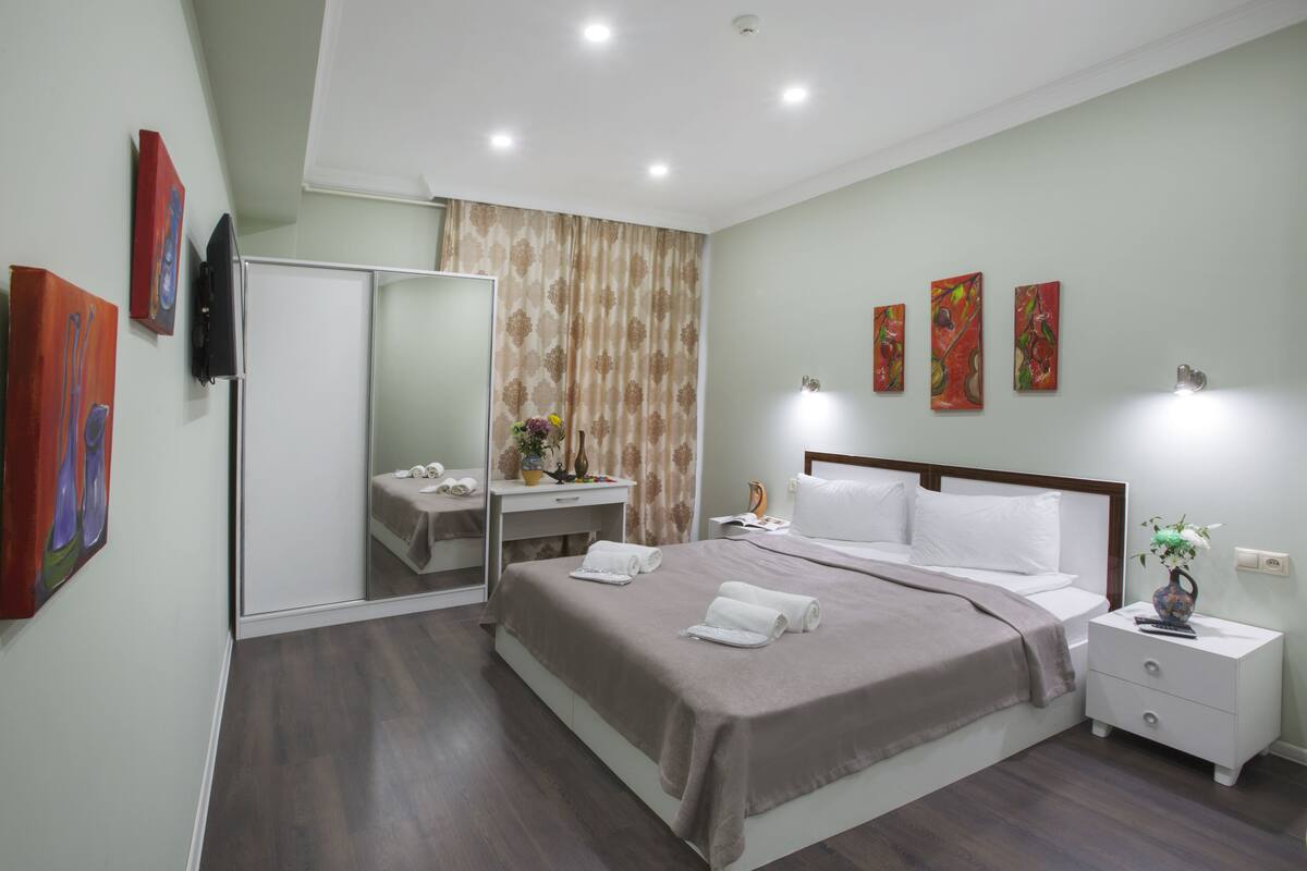 Une chambre à coucher moderne avec un grand lit, des tables de chevet, un miroir et des œuvres d’art accrochées aux murs.