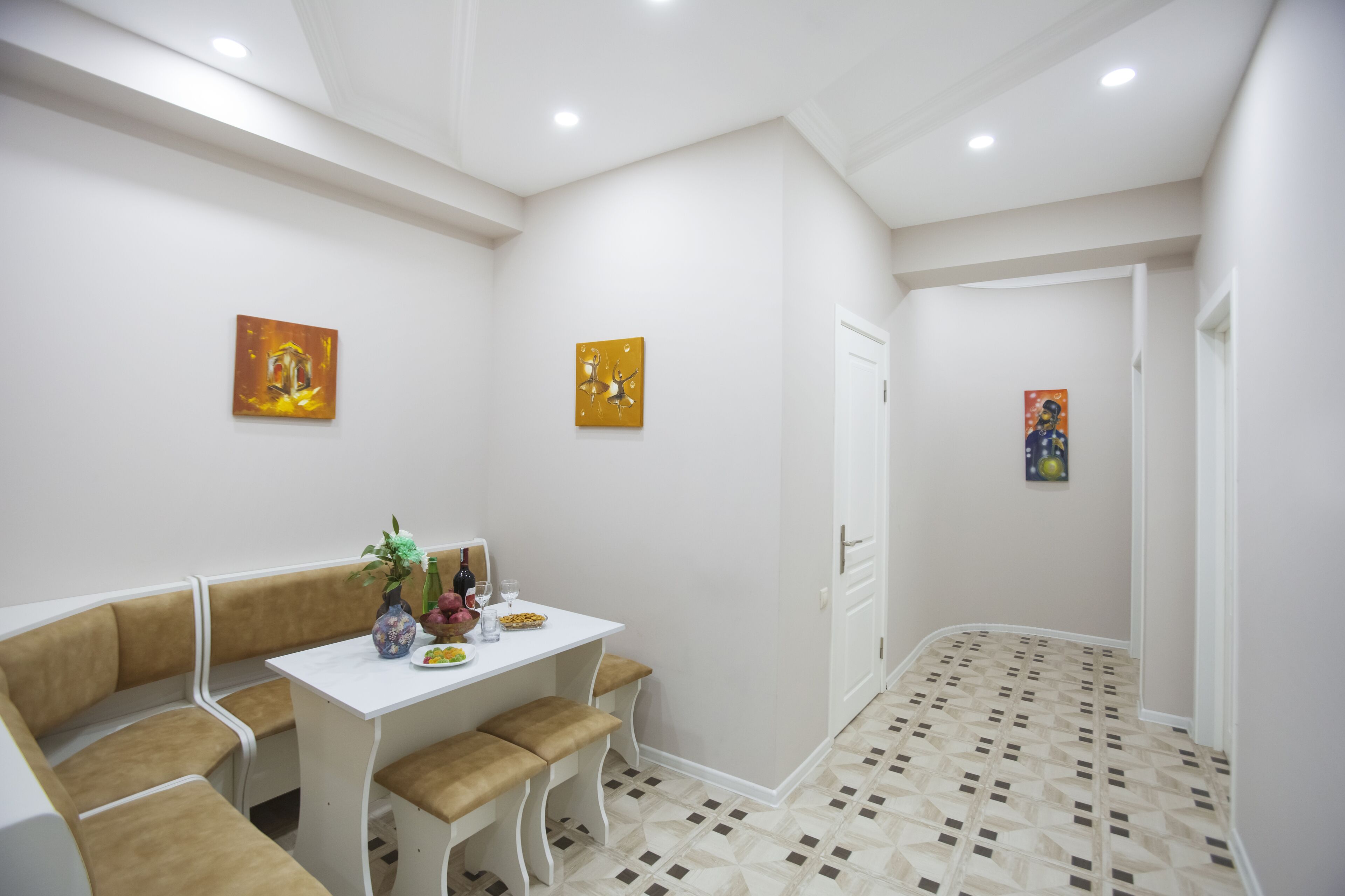 A dining area with a white table and bench seating, a vase with flowers, and two paintings on the wall.
