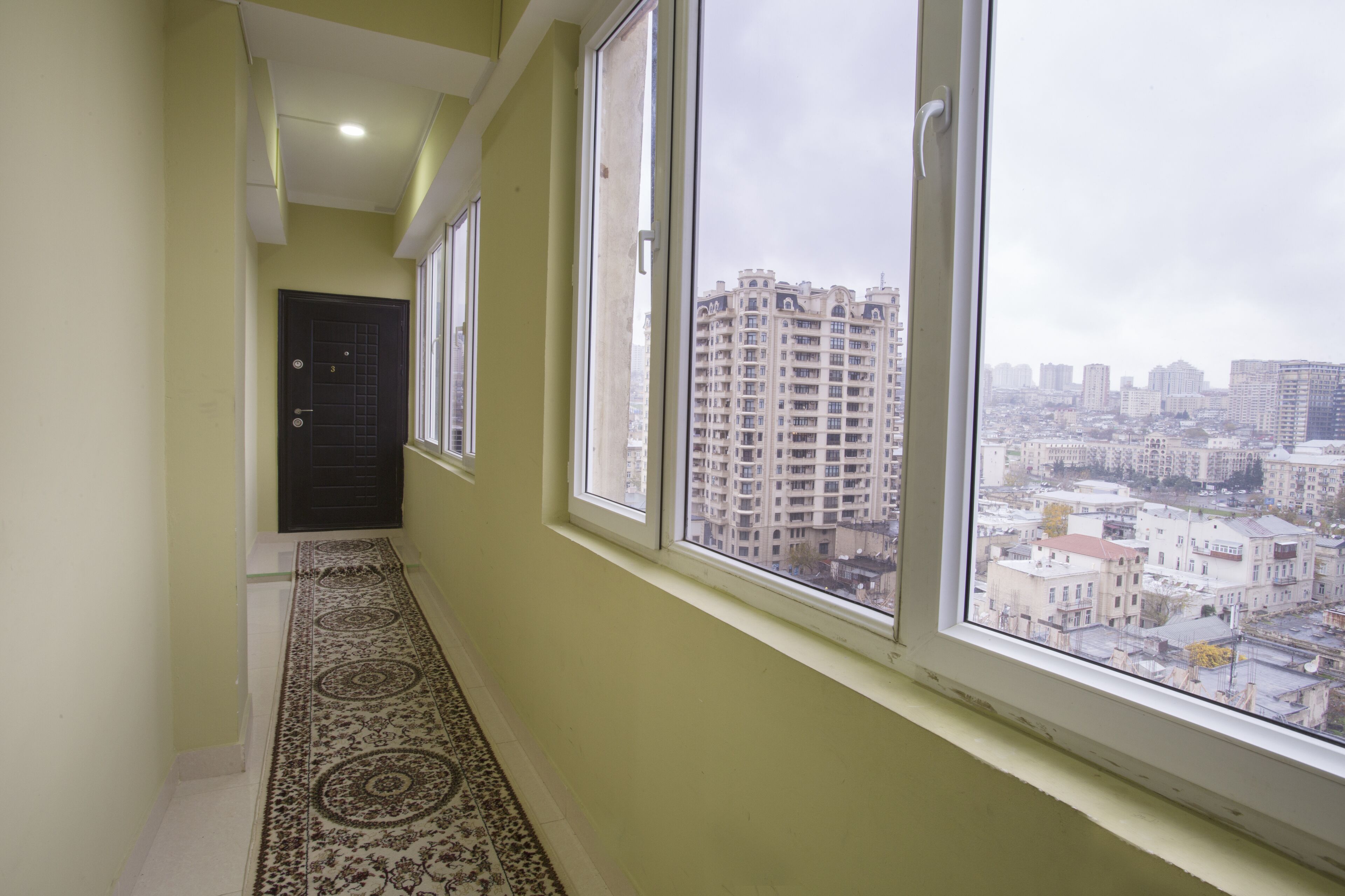 A corridor with large windows, a patterned carpet, and a view of a cityscape with high-rise buildings.