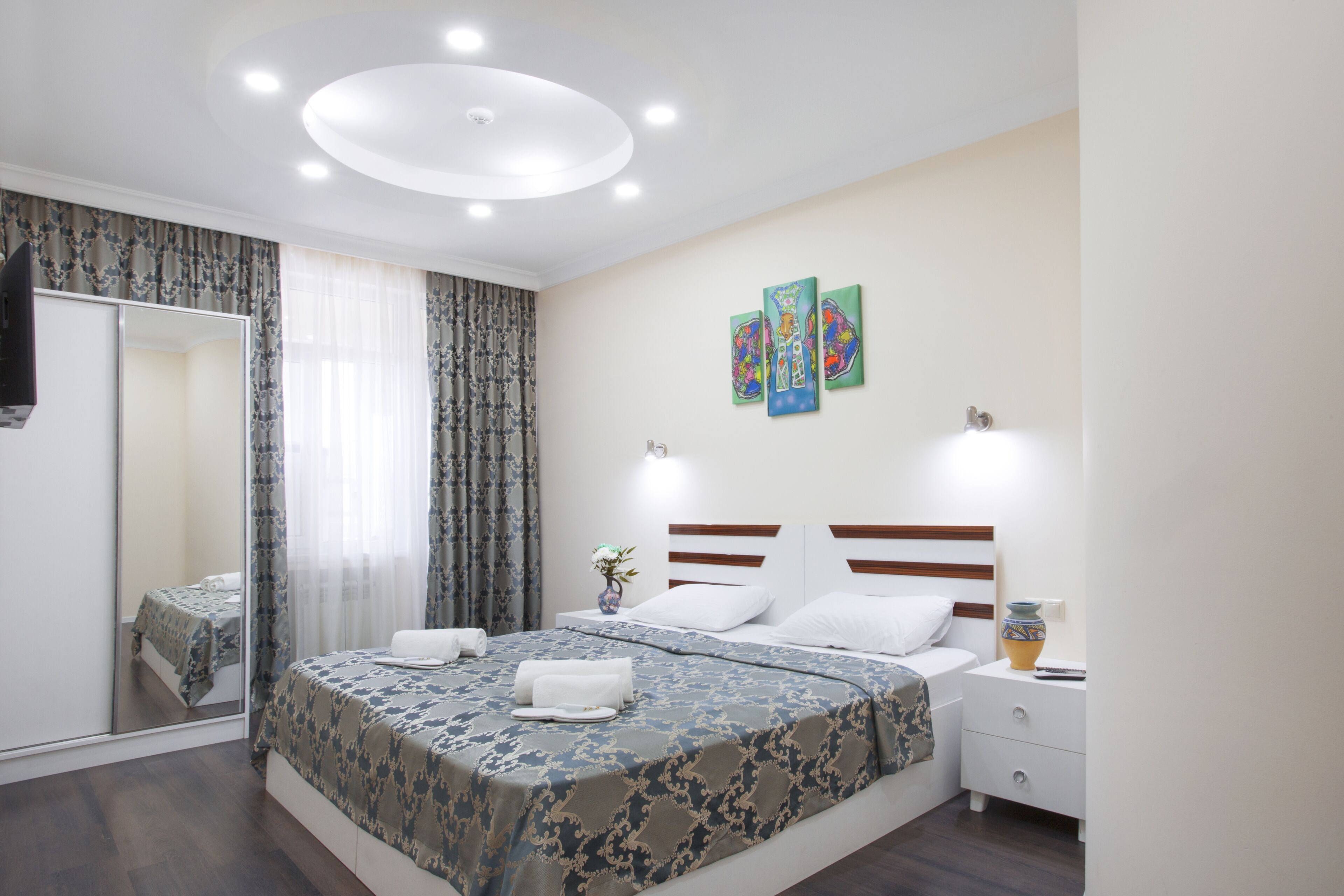 A hotel room with a large bed, a bedside table with a vase, and a mirror.