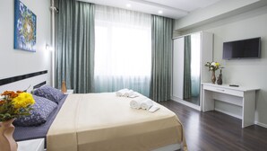 Una habitación de hotel moderna con una cama, un escritorio, un televisor de pantalla plana y un ventanal con cortinas.