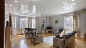Amplia sala de estar con techo alto, piso de madera, zona de estar central con sofás y sillones, una mesa de comedor y un televisor.