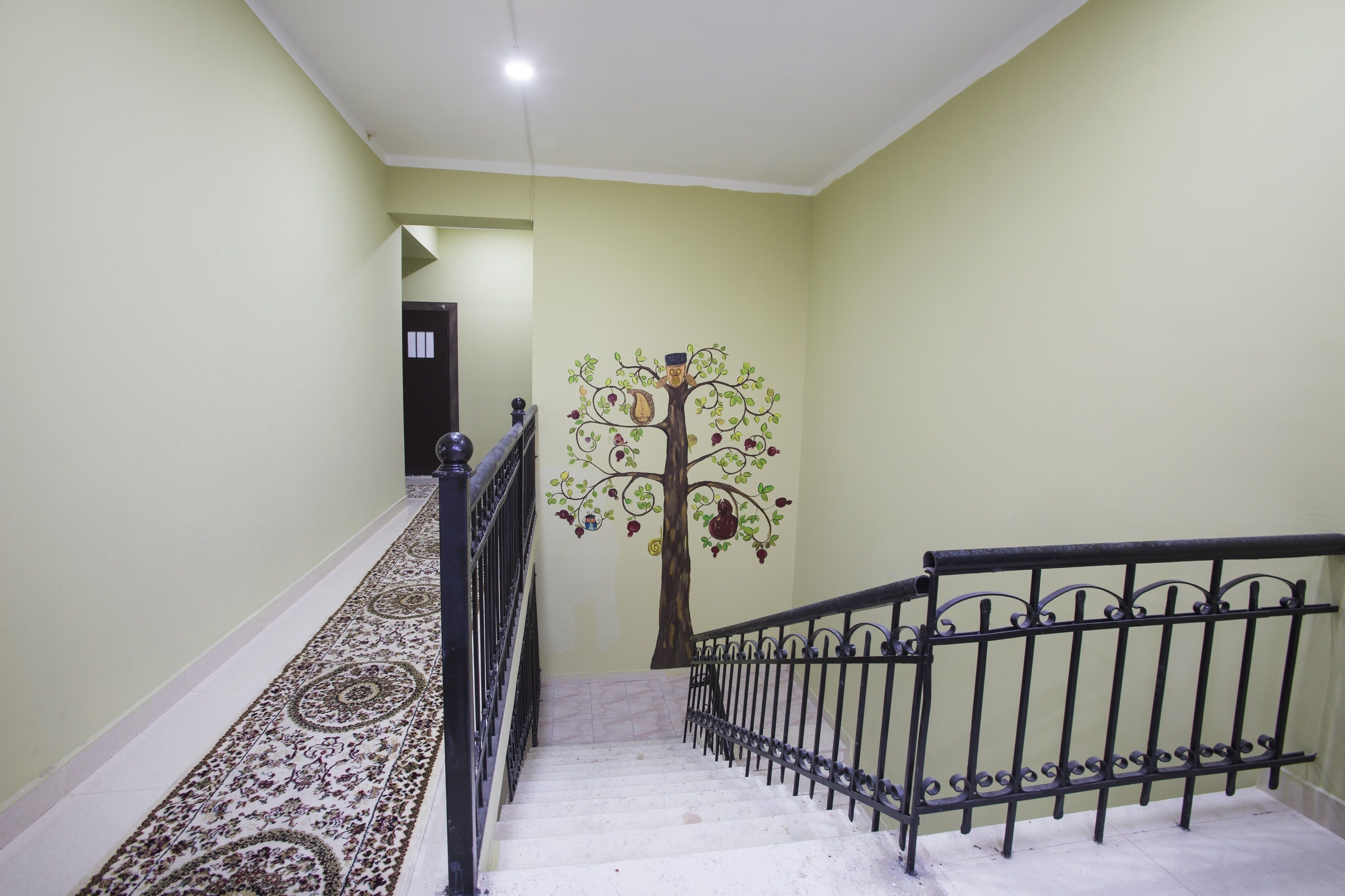 Un escalier orné d’une fresque représentant un arbre sur le mur, un tapis à motifs et une rampe en métal.
