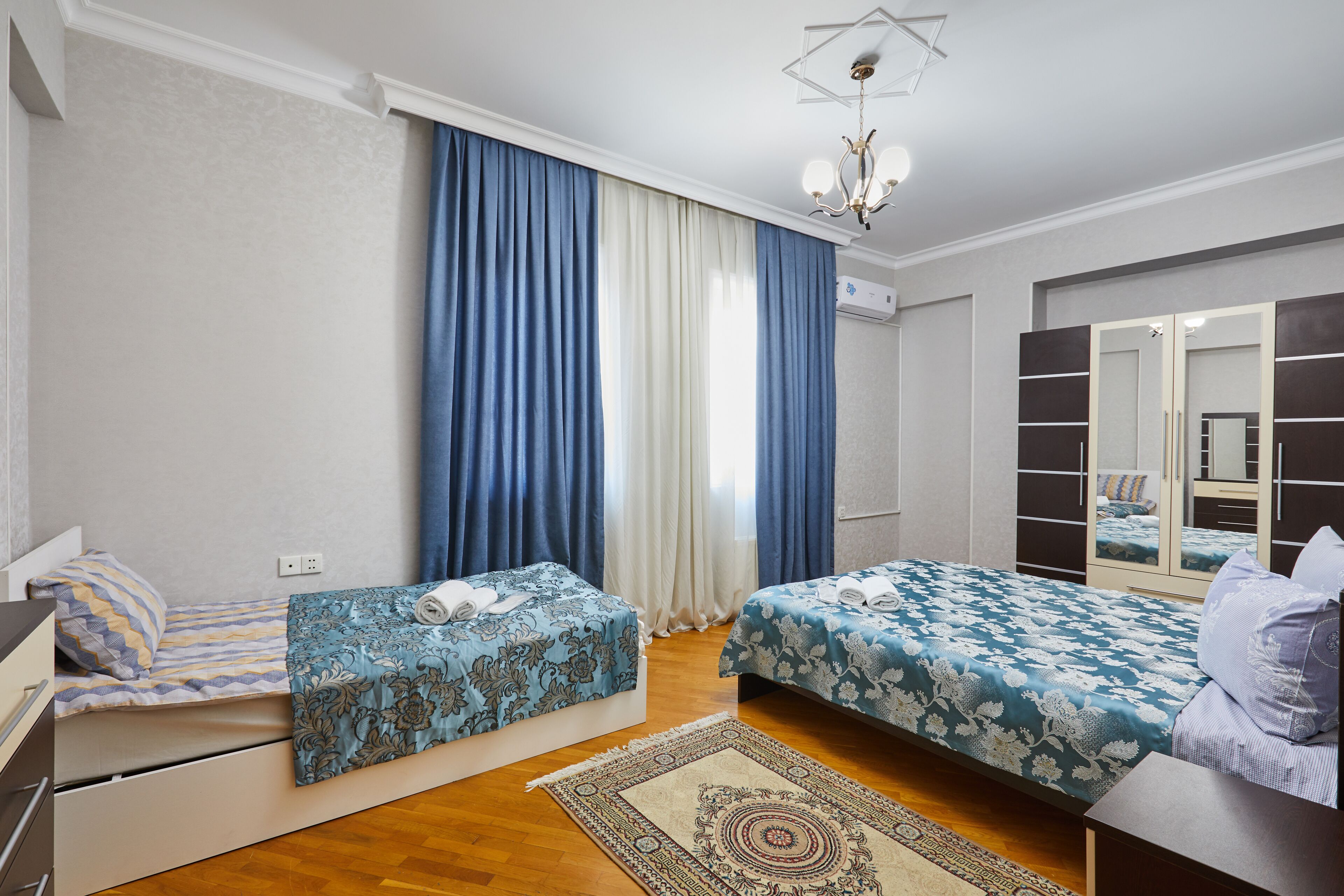 A bedroom with two beds, a large mirror, and a chandelier.