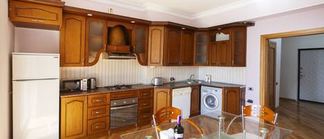A modern kitchen with wooden cabinets, a glass dining table, and a stainless steel refrigerator.