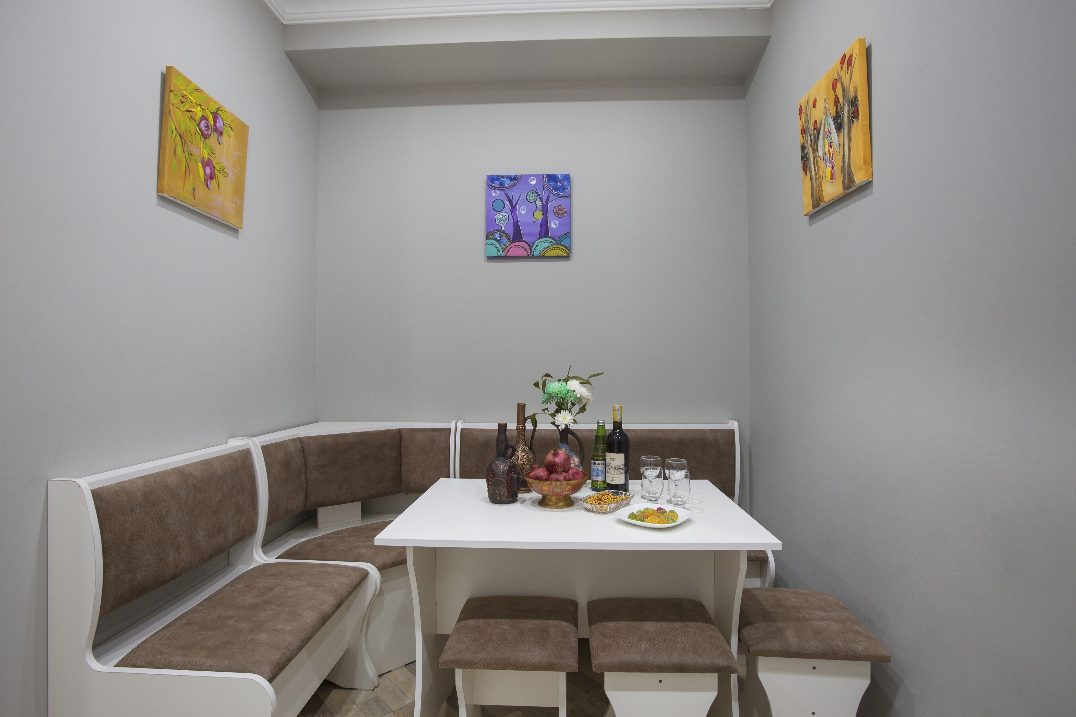 Un comedor con una mesa blanca, bancos acolchados color café y dos cuadros en las paredes.