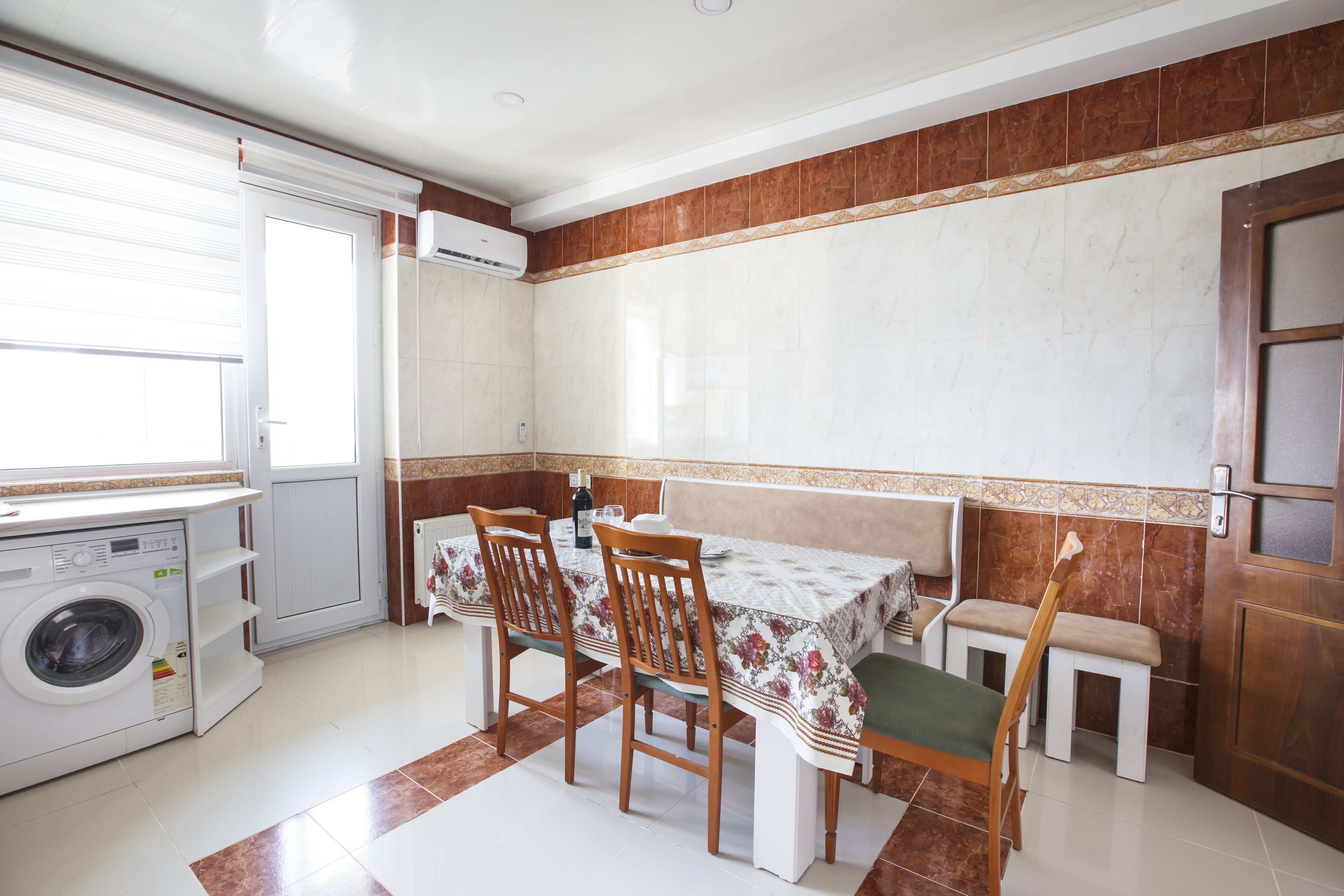 A compact kitchen with a washing machine, dining table, chairs, and a bench.
