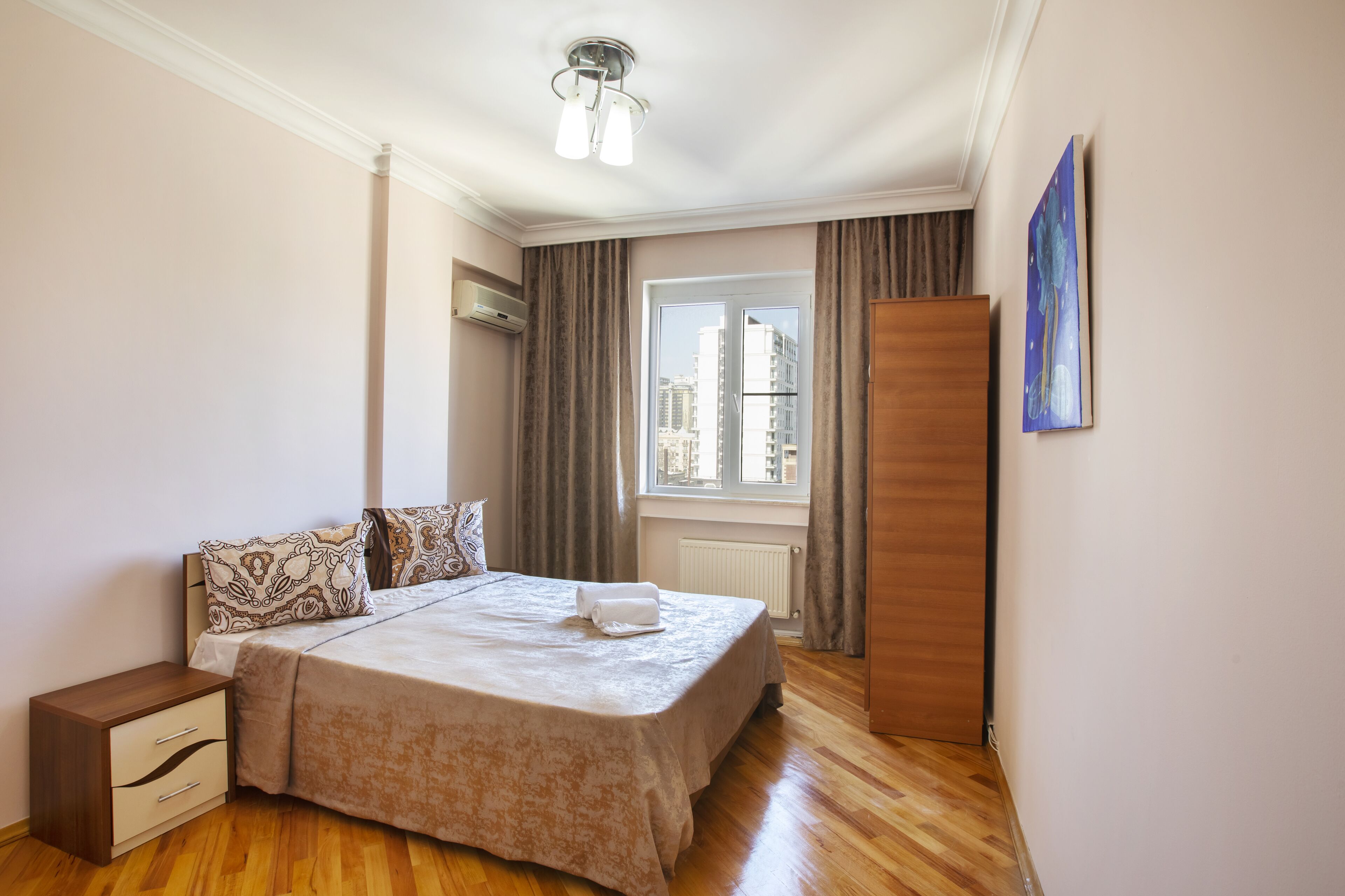 Un dormitorio ordenado con cama, mesita de noche y ventana con cortinas.