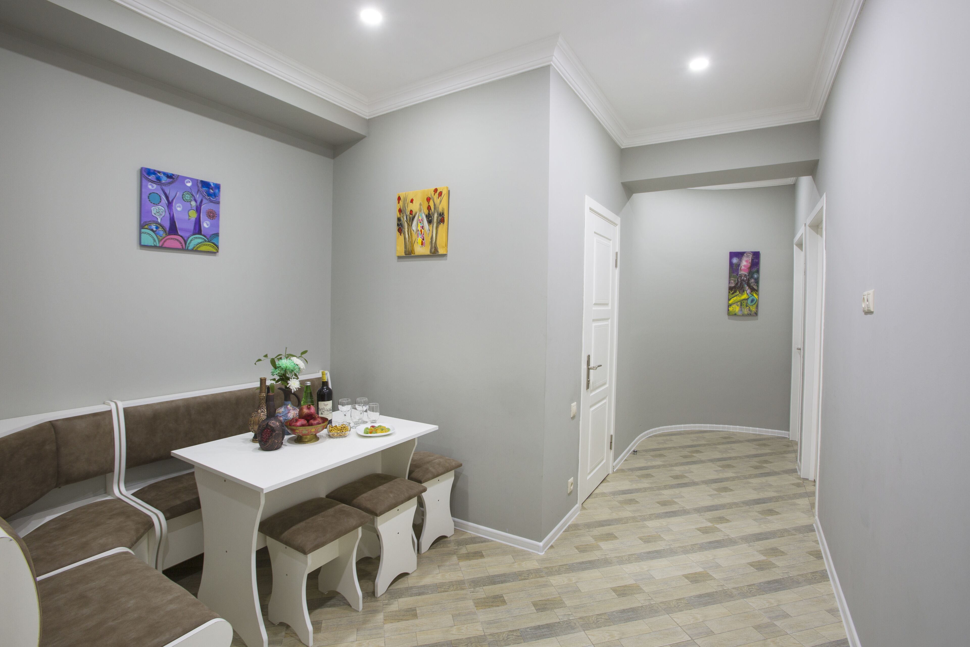 A dining area with a white table and bench seating, a small decorative vase, and a fruit bowl.