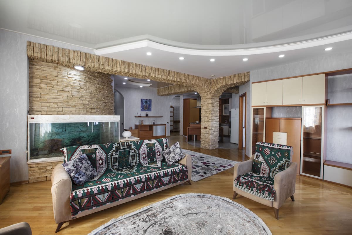Un salon spacieux avec un grand aquarium, un canapé agrémenté de coussins à motifs et un fauteuil recouvert d’un plaid décoratif.