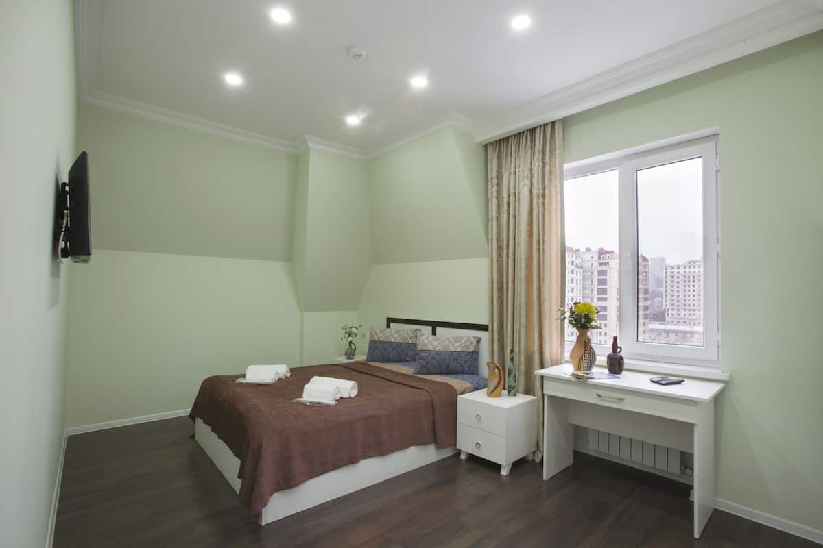 Une chambre à coucher avec un lit, une table de chevet et une fenêtre donnant sur des immeubles.