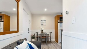 En moderne stue med sofa, spisebord med stole, et køkkenområde og et stort spejl.