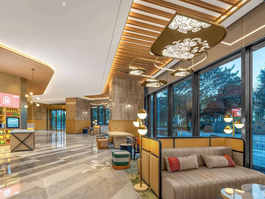 A modern lobby with a seating area, a reception desk, and large windows offering a view of the outdoors.