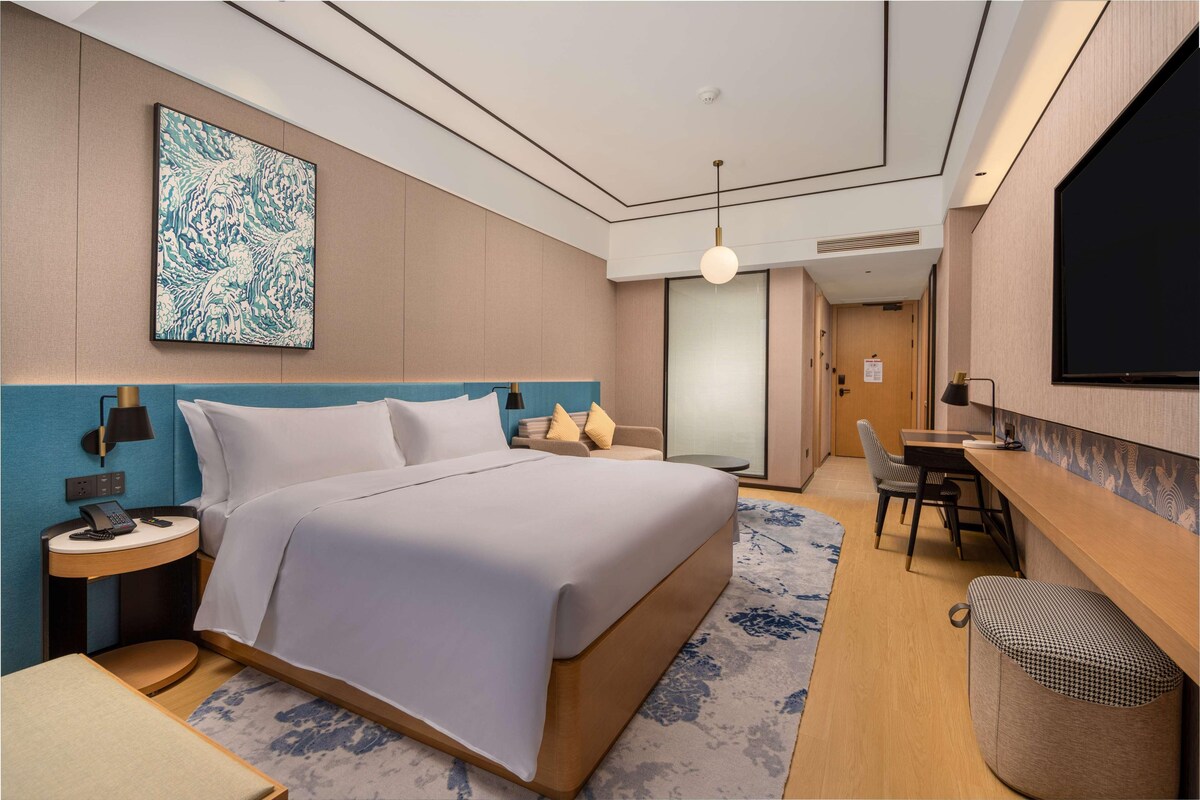 Una habitación de hotel con cama, mesita de noche, lámpara y un escritorio con silla.