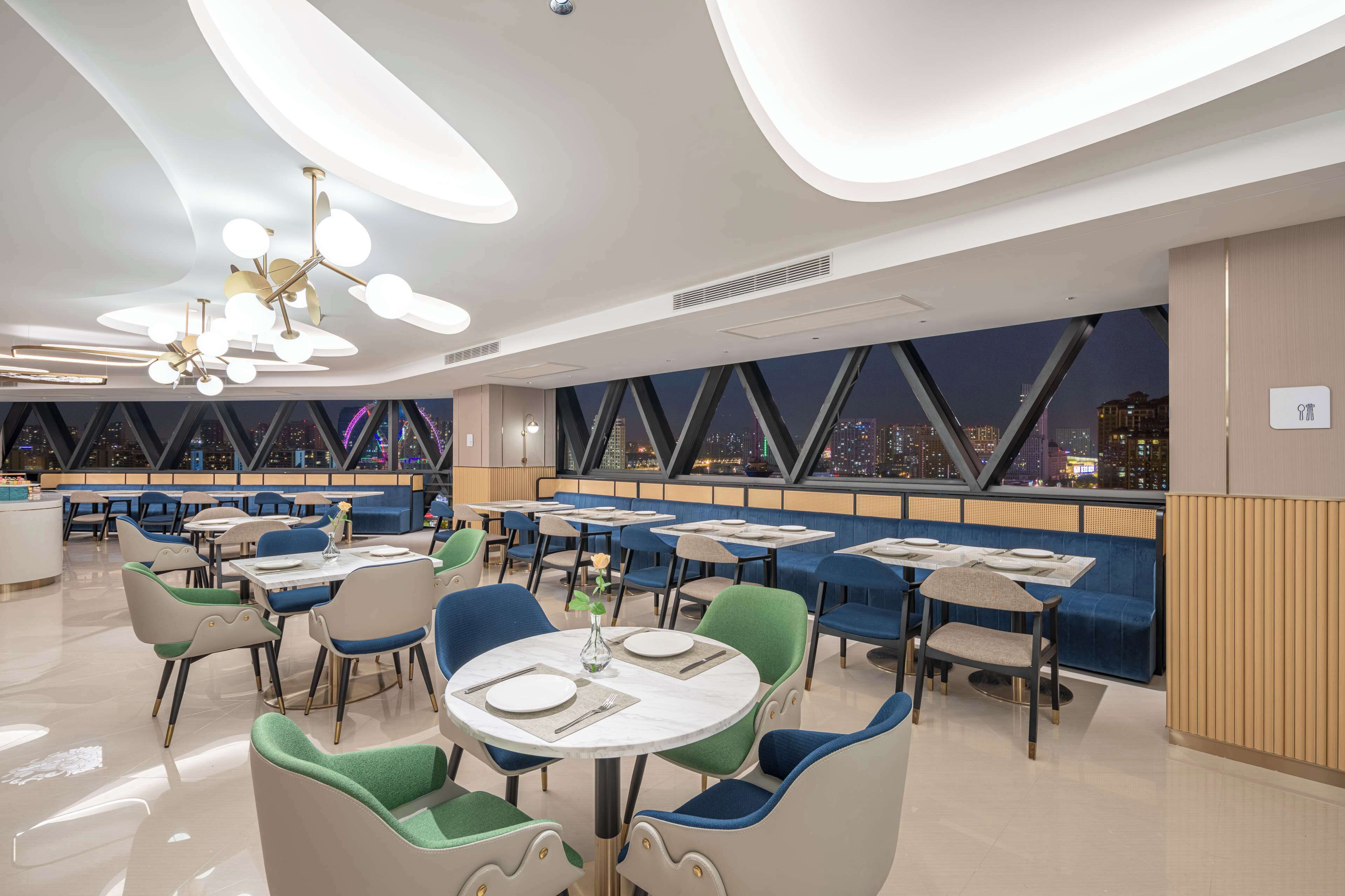 A modern restaurant with round tables and chairs, a city view through large windows, and a ceiling with circular light fixtures.