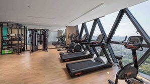 Un gimnasio con cintas de correr, elípticas y máquinas de pesas, ventanas amplias con vista a la ciudad.