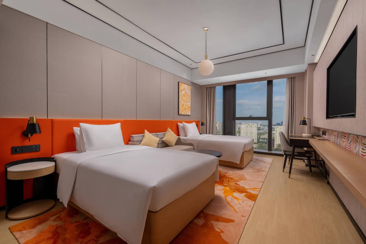 A modern hotel room with two beds, a desk, a chair, a TV, and a large window offering a city view.