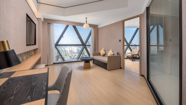 Una sala de estar moderna con un sofá, una mesita de centro y una silla. Se ve un ventanal con vistas a la ciudad.