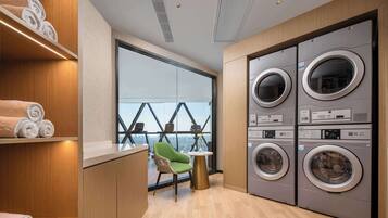 A modern laundry room with stacked washing machines, a green chair, and a view through large windows.