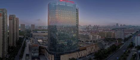 A modern hotel with a distinctive geometric facade, surrounded by urban buildings and a clear sky.