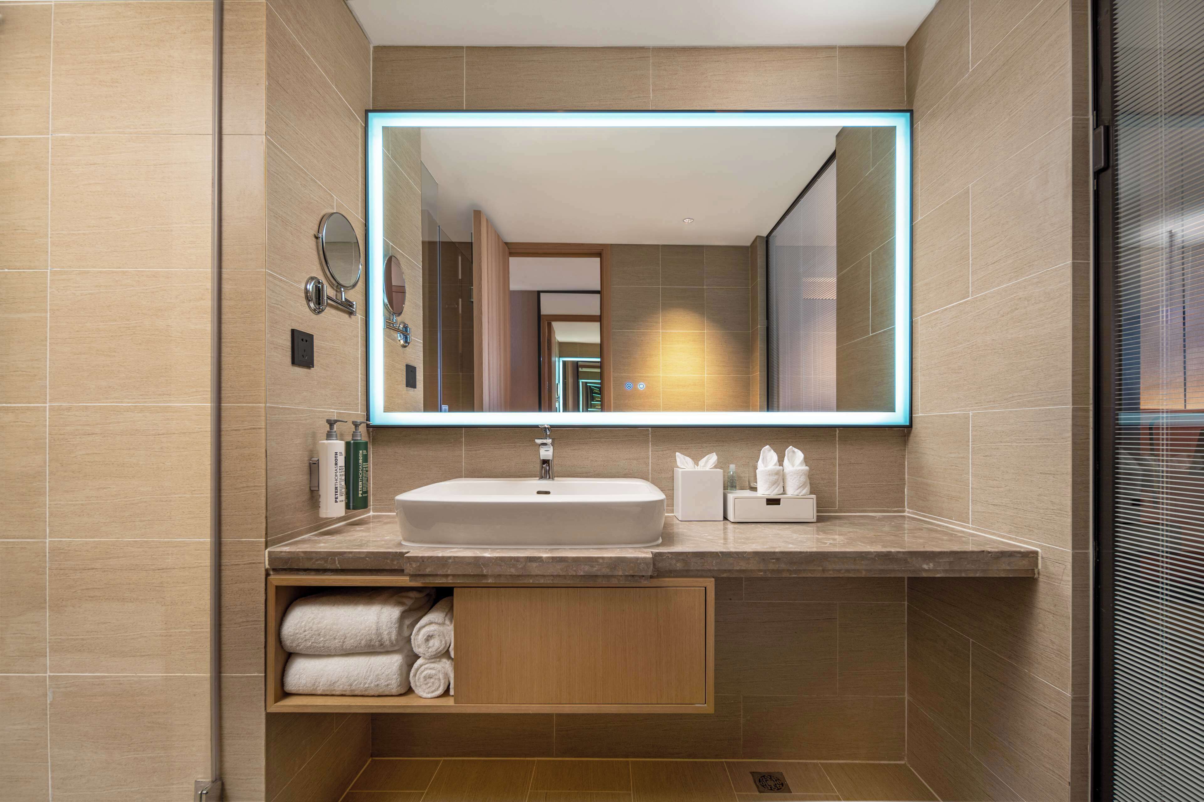 A modern bathroom with a large mirror, a sink, and a towel rack.