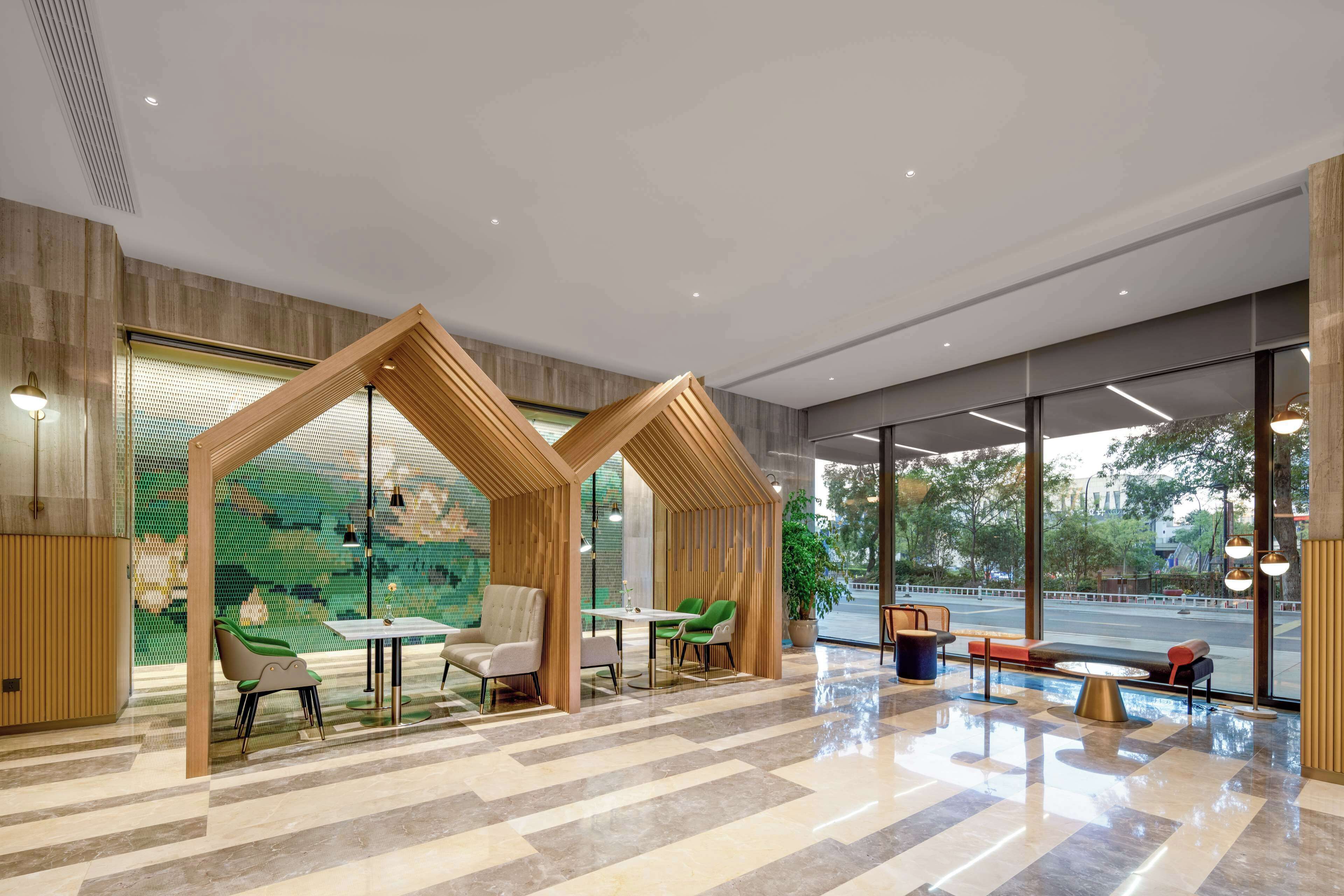 Un vestíbulo moderno con una estructura de madera geométrica, asientos y grandes ventanales con vista a la calle.