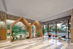 Un vestíbulo moderno con una estructura de madera geométrica, asientos y grandes ventanales con vista a la calle.