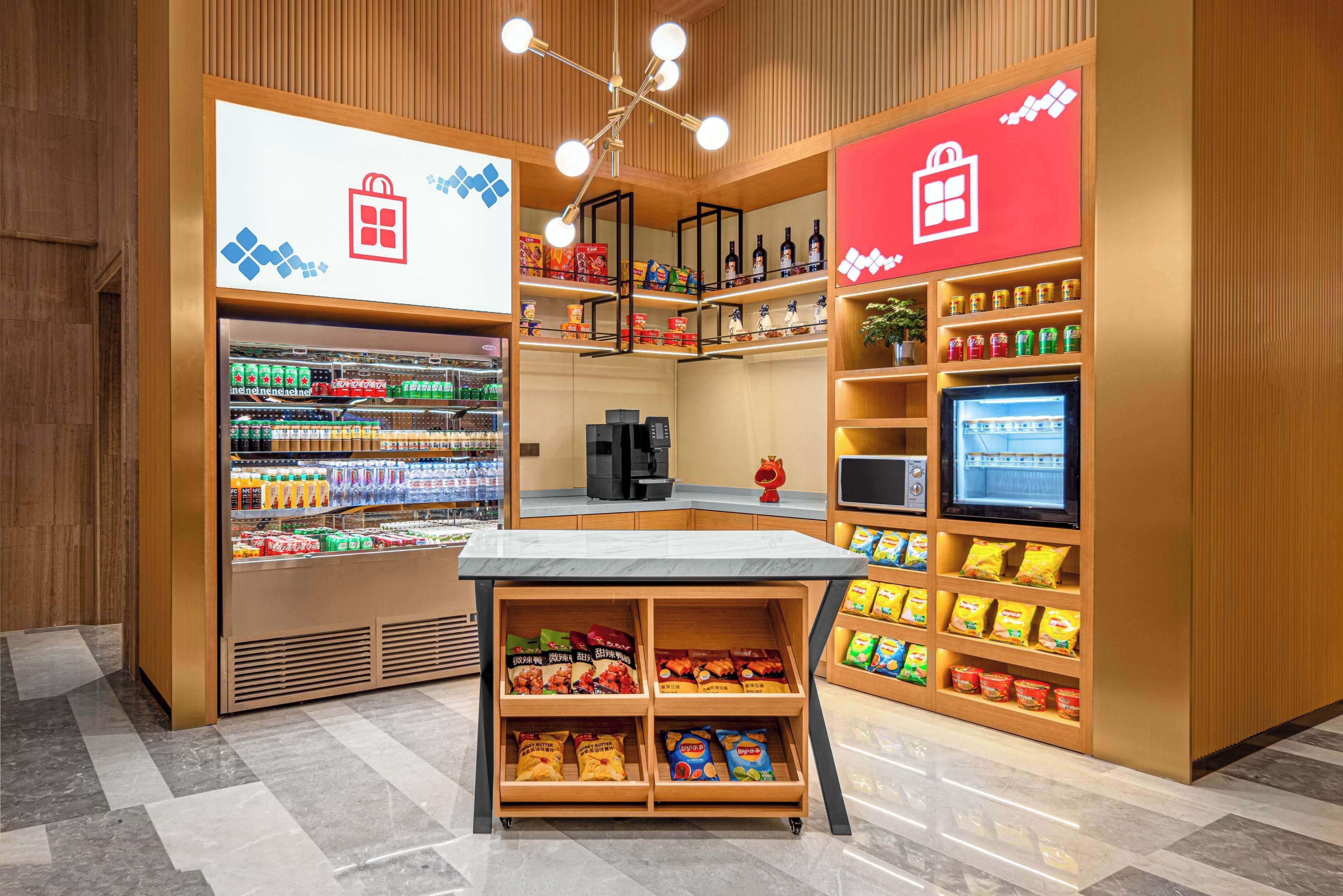 Ein gut beleuchteter Imbissstand mit Regalen voller Snacks und Getränke, einer Kaffeemaschine und einem digitalen Bildschirm.